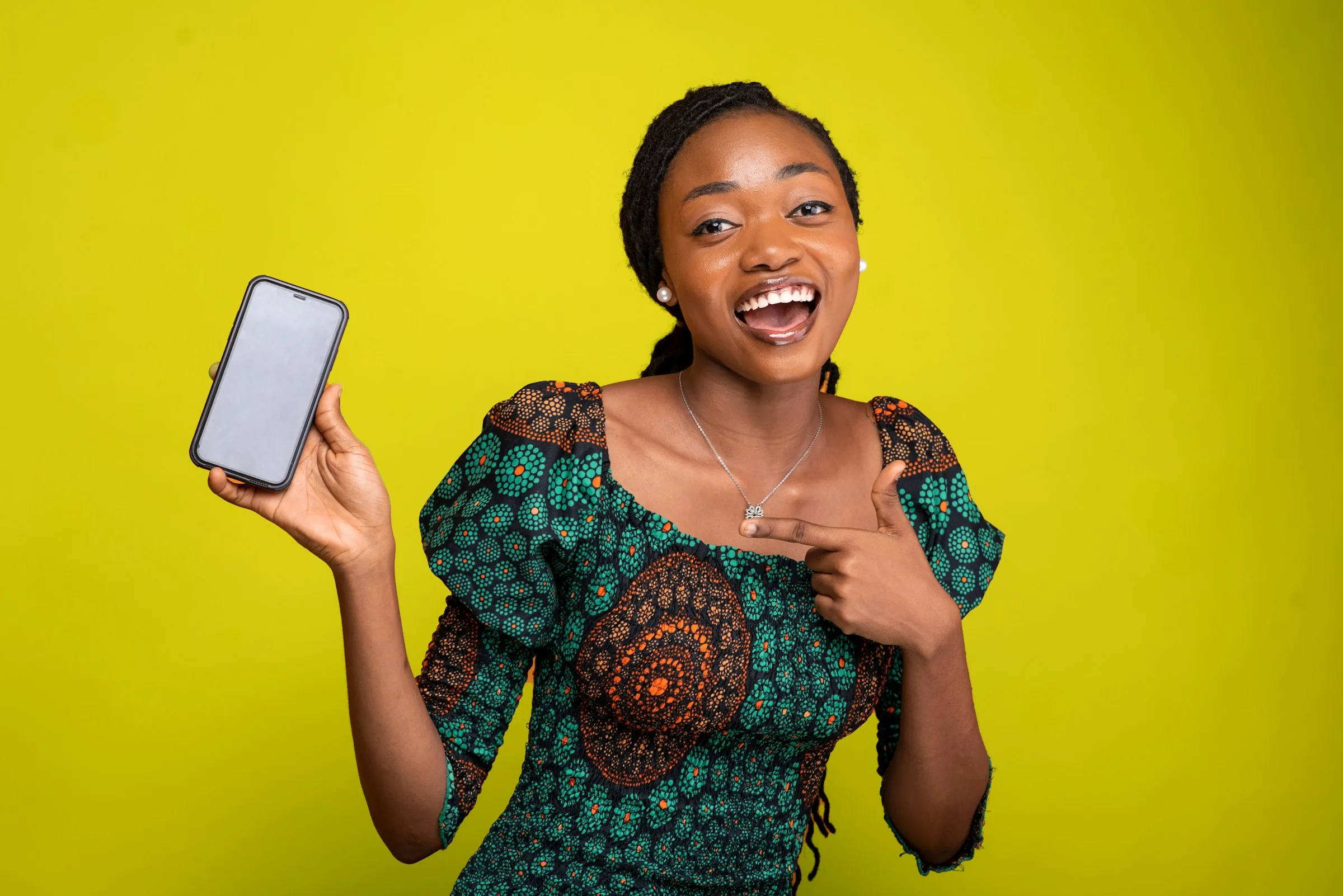 A smiling woman holding up her phone against a yellow backdrop